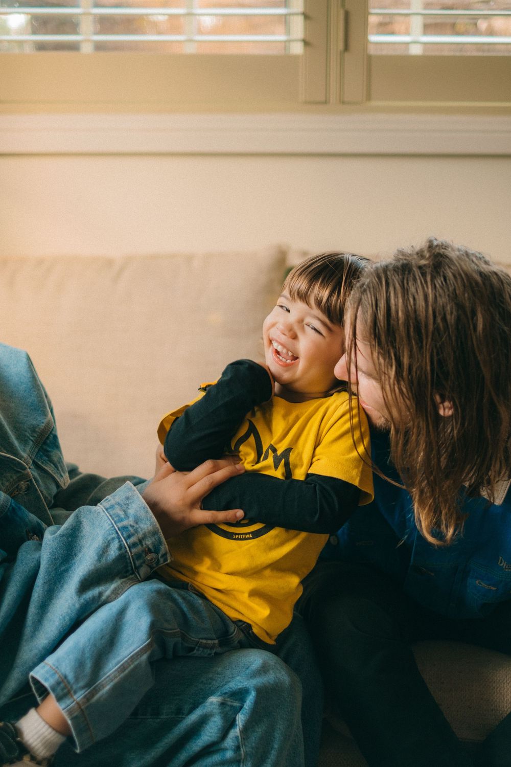 Joyful playtime moment shared on a comfortable beige sofa in a sunlit room.
