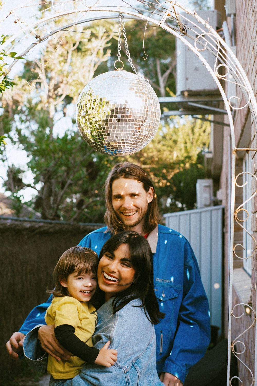 A family poses together under a disco ball in a backyard garden setting.