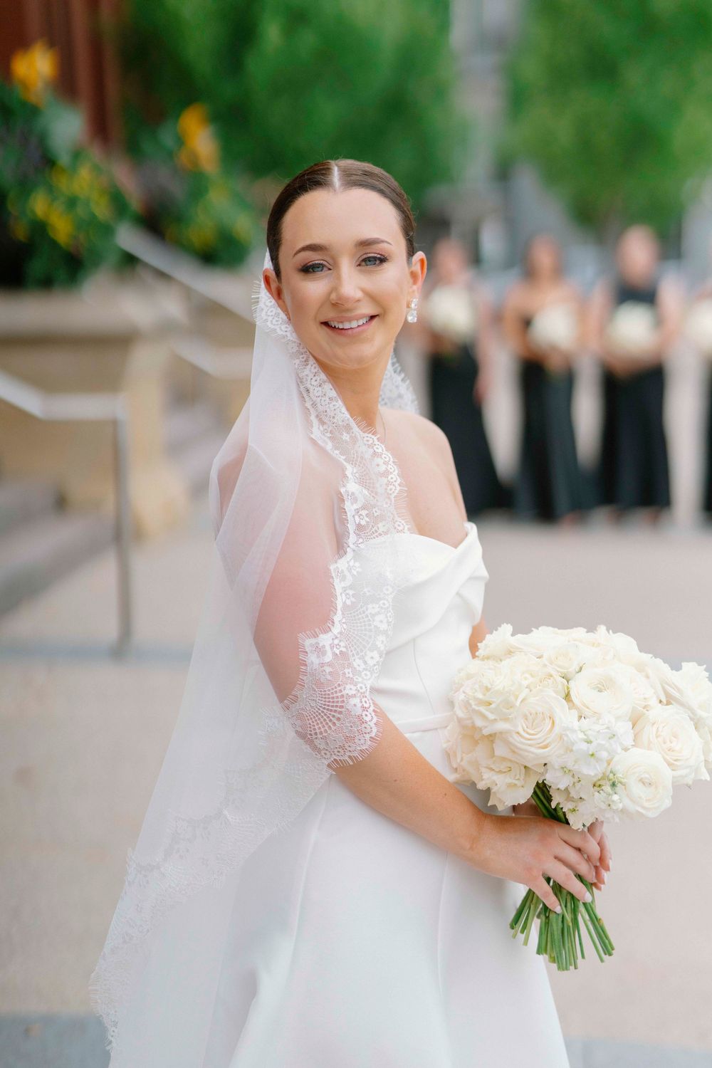 A bride in a white wedding dress holds an elegant bouquet of cream roses with a delicate lace-trimmed veil.