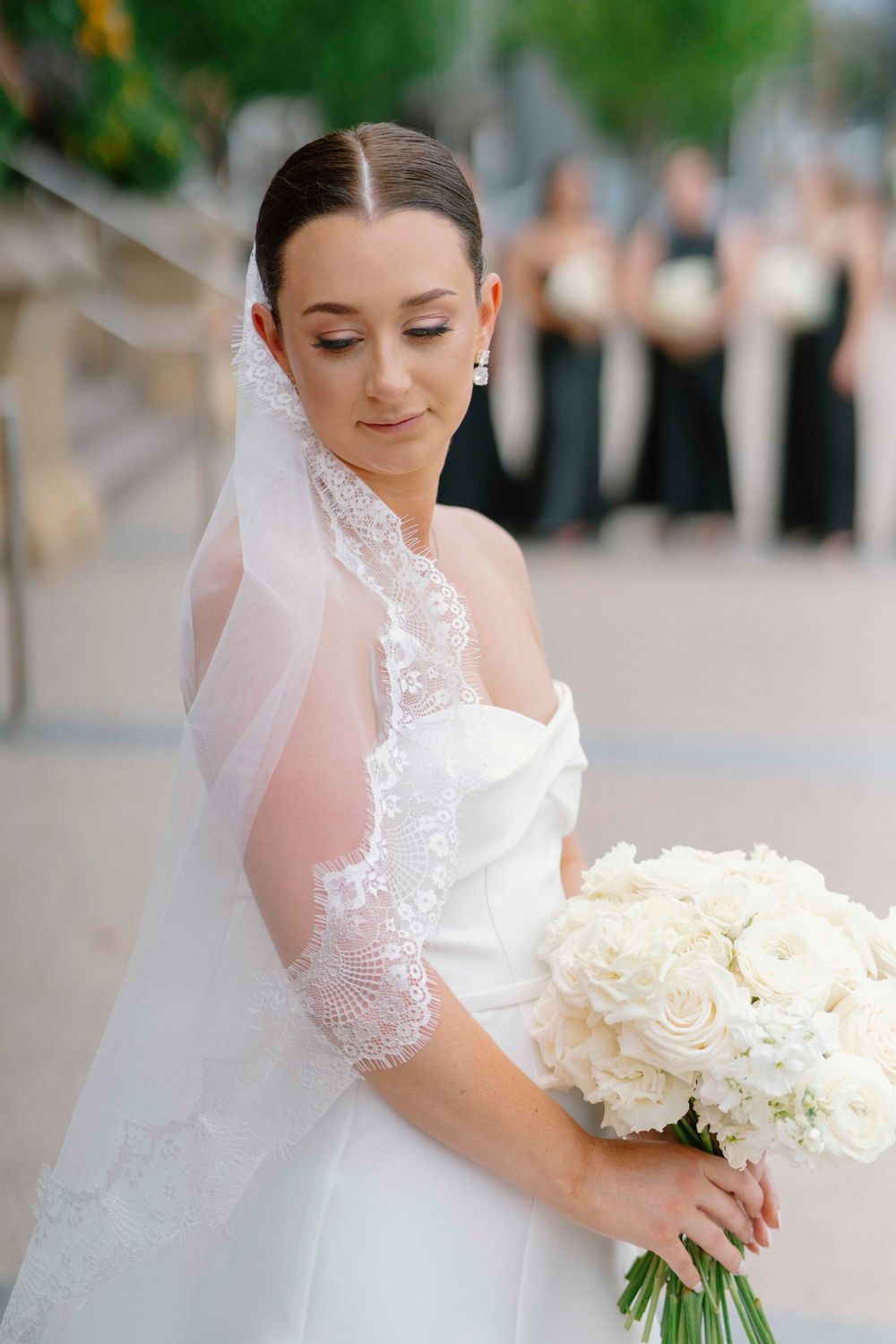 Close-up views of a bride holding a classic white rose bouquet while wearing a lace-detailed veil.