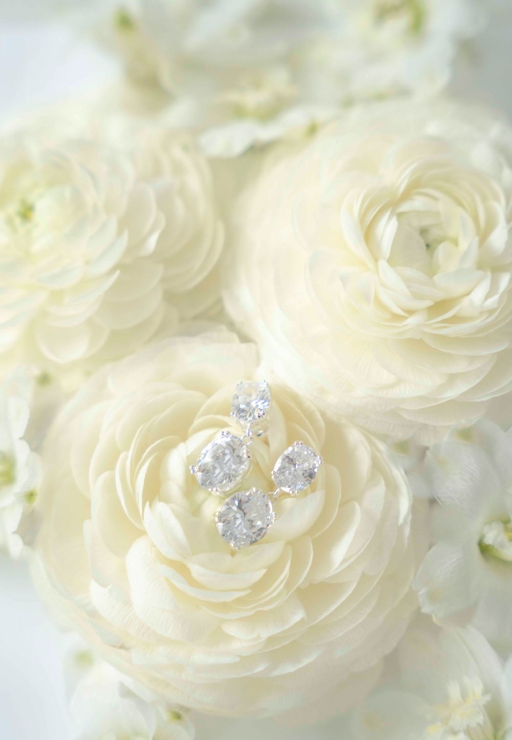 Delicate white ranunculus flowers with sparkling diamond jewelry nestled in soft petals create an elegant bridal arrangement.