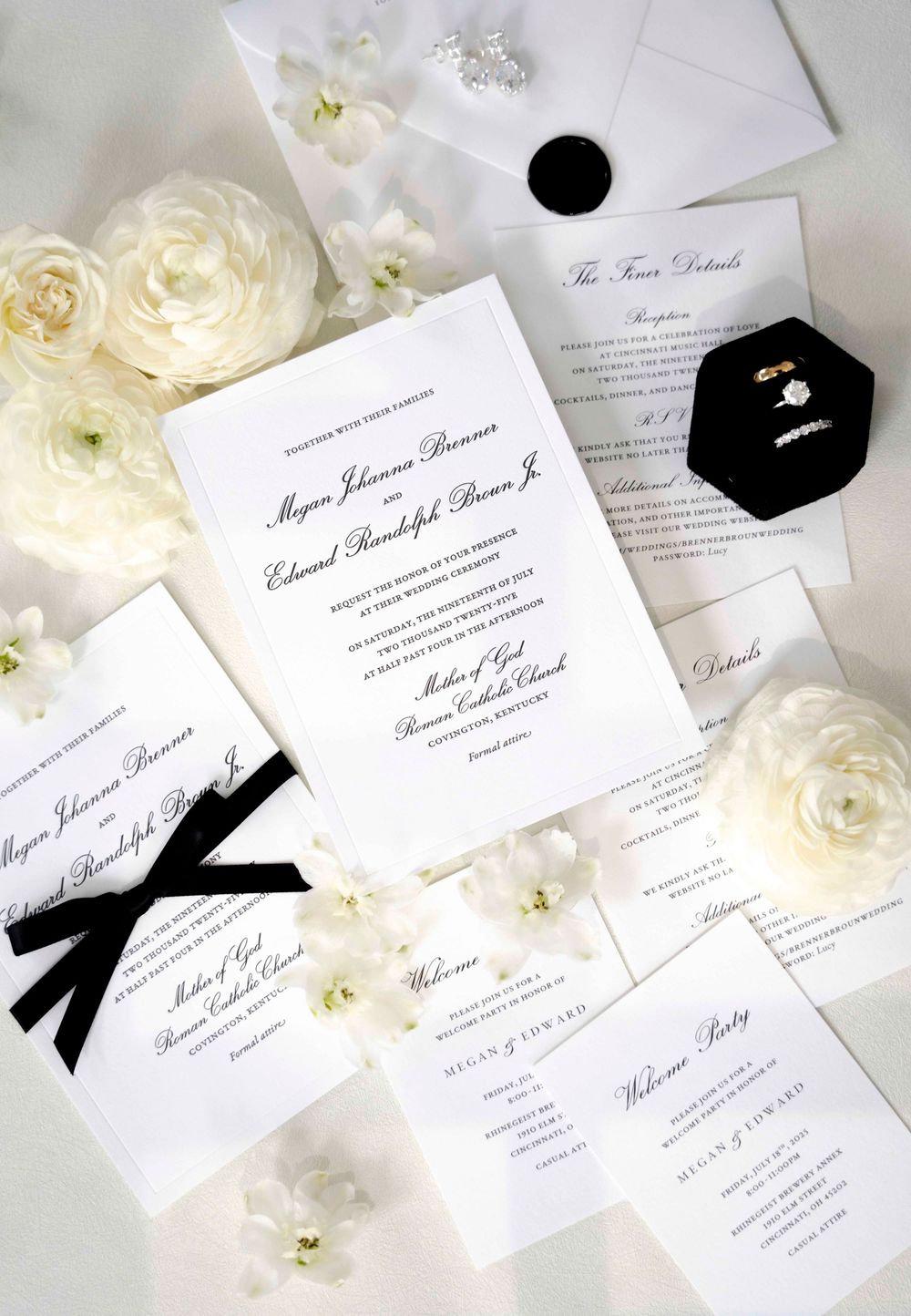 Elegant black and white wedding invitations with calligraphy alongside delicate white roses and silk ribbons.