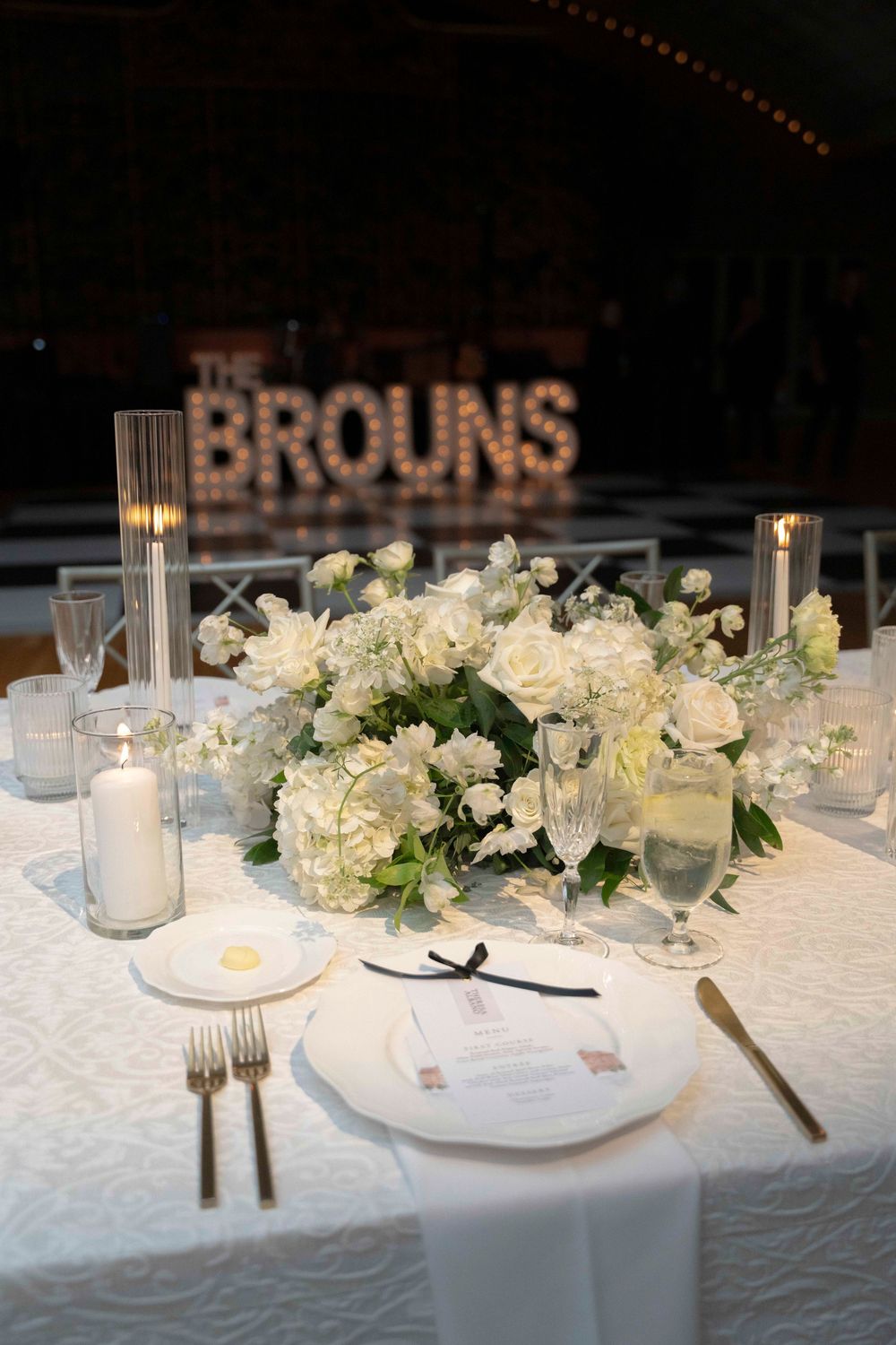 Wedding reception table with 'THE BROUNS' signage, white floral centerpiece and formal place settings.