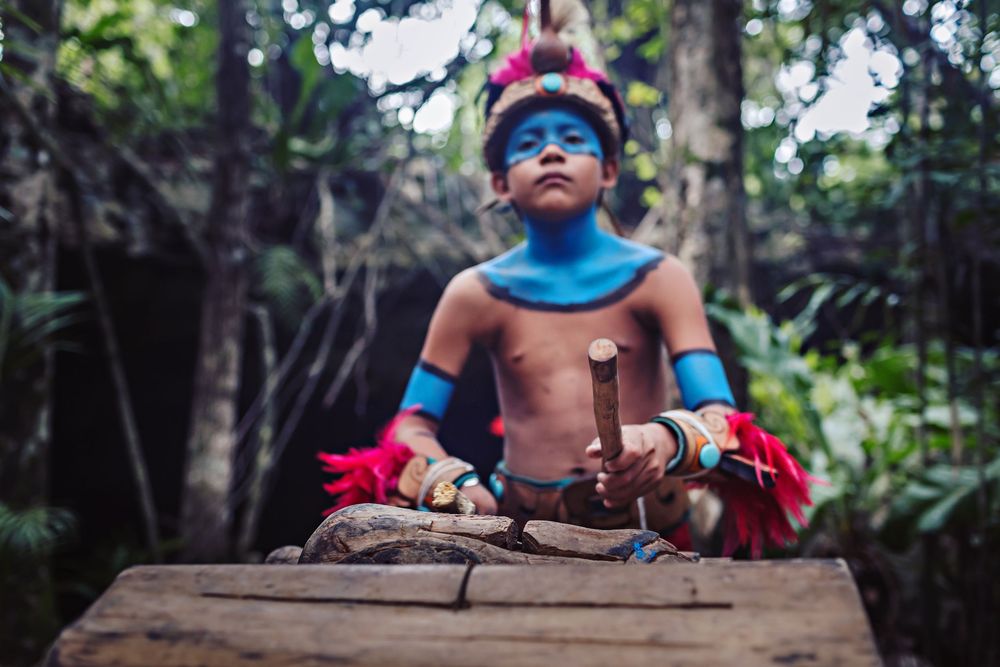 Young boy in traditional Mayan attire playing ceremonial drums in a jungle elopement ceremony.