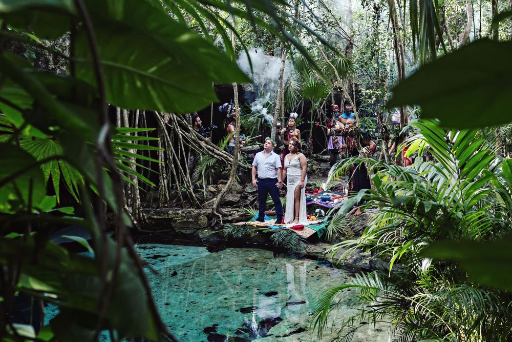 Wide view of a Mayan wedding ceremony by a crystal-clear cenote surrounded by nature.