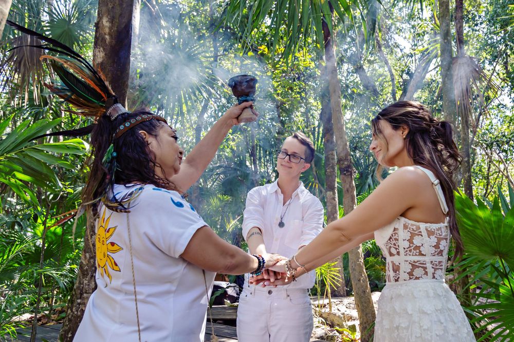 A tropical garden wedding ceremony with couples holding hands surrounded by lush greenery and palm trees.