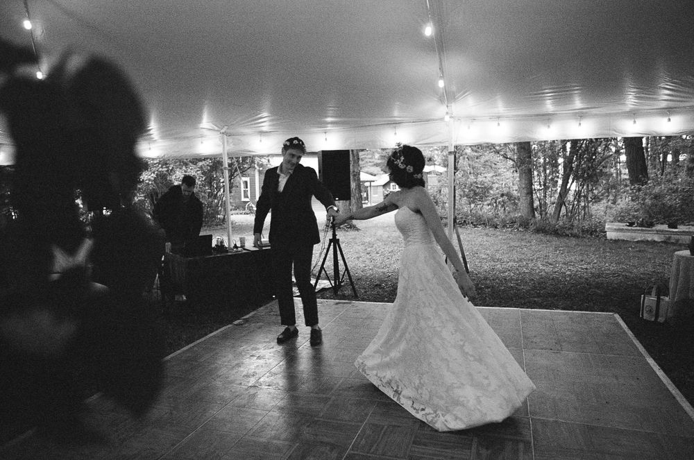 Black and white photo of couple dancing on wooden floor under wedding tent.