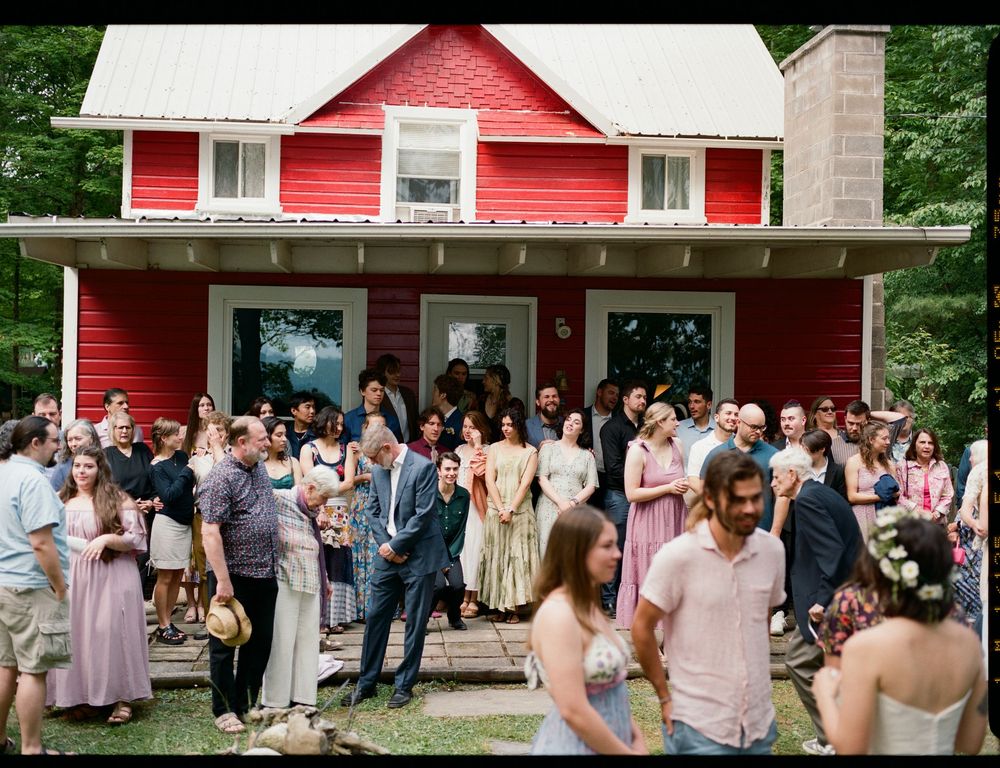 Wedding guests gathered outside a charming red farmhouse for a celebration.