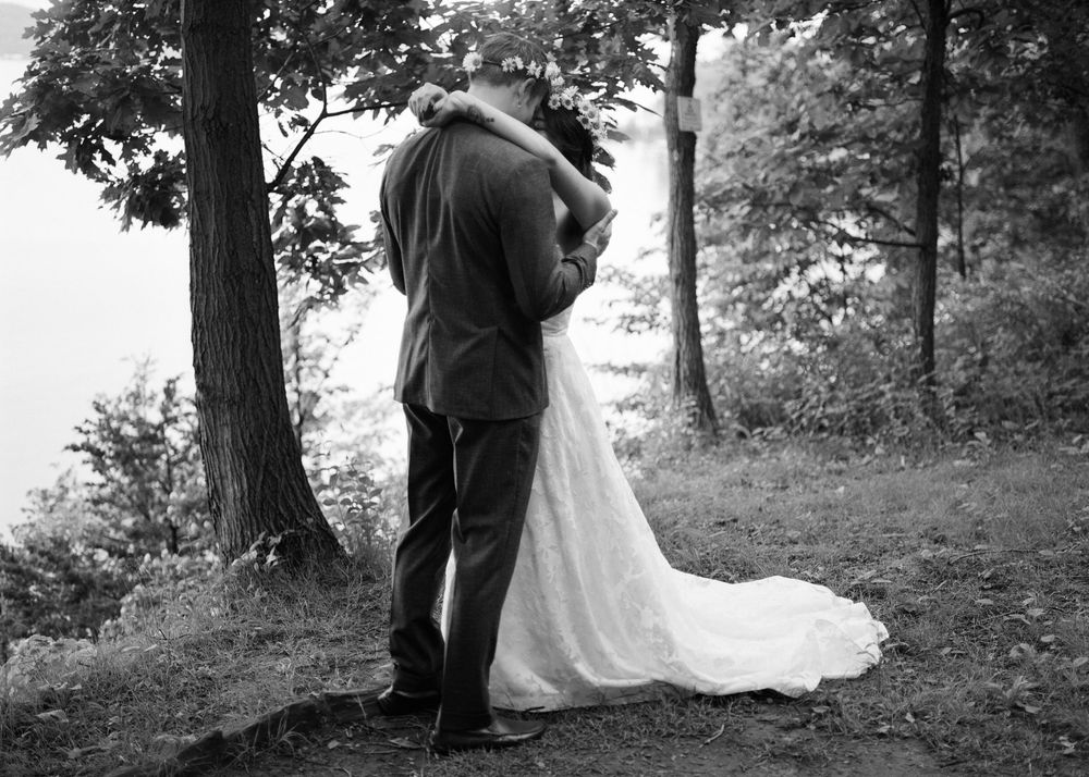 A black and white wedding photograph shows a tender embrace among trees.