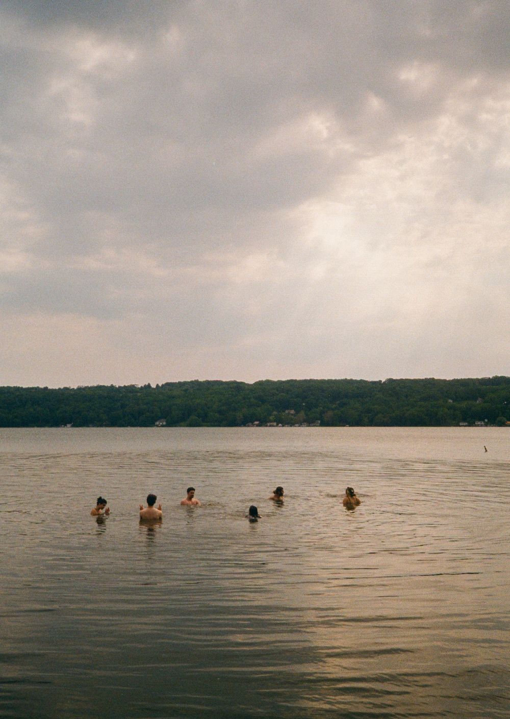 People swimming in a calm lake under a dramatic cloudy sky at dusk.