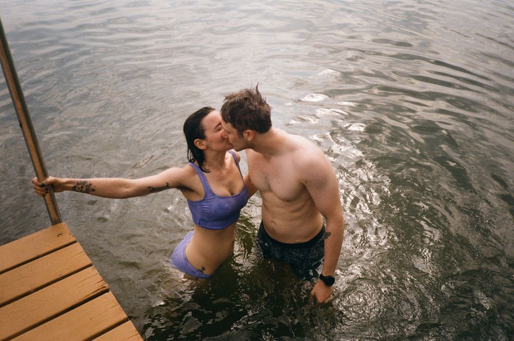 People swimming and sitting on a wooden dock by calm water during a peaceful summer afternoon.