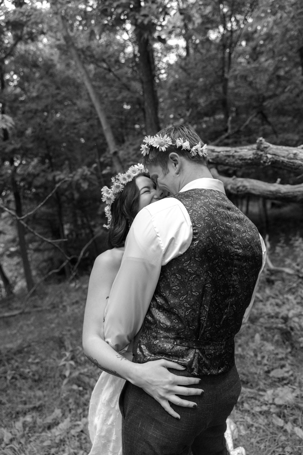 Intimate black and white wedding photo of couple embracing in forest setting.