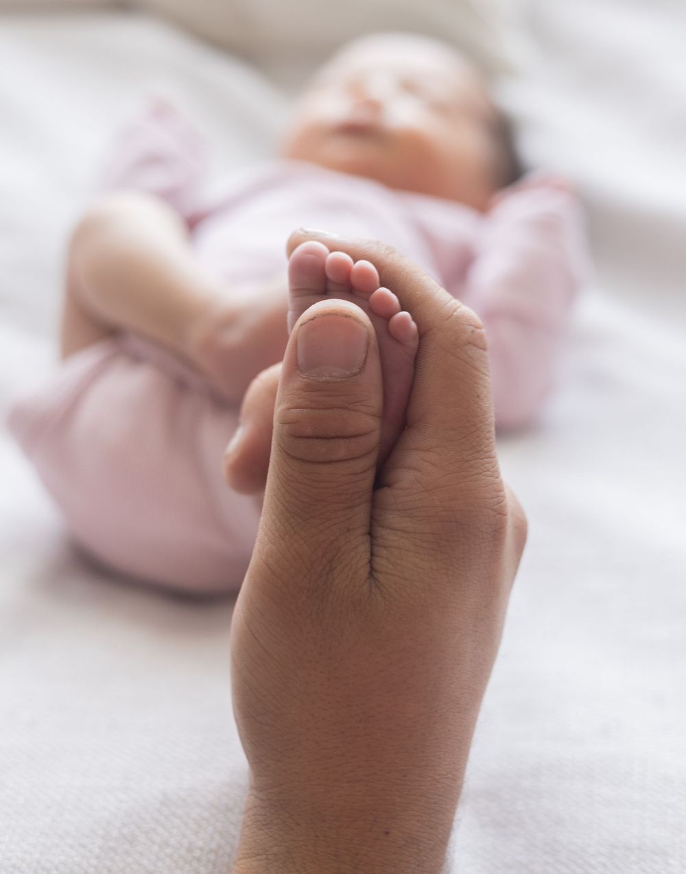 A tiny baby foot being gently held by an adult hand against a soft white background.