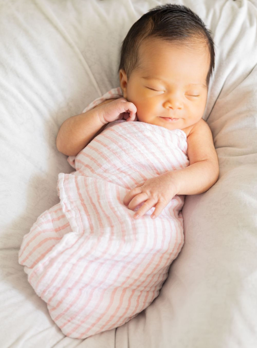 Five connected images show a sleeping baby in pink striped clothing laying on white bedding at different angles.
