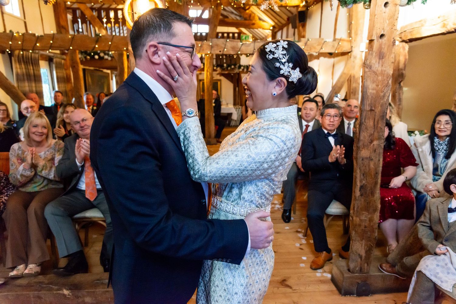 A couple shares an intimate dance together at their rustic barn wedding venue surrounded by seated guests.