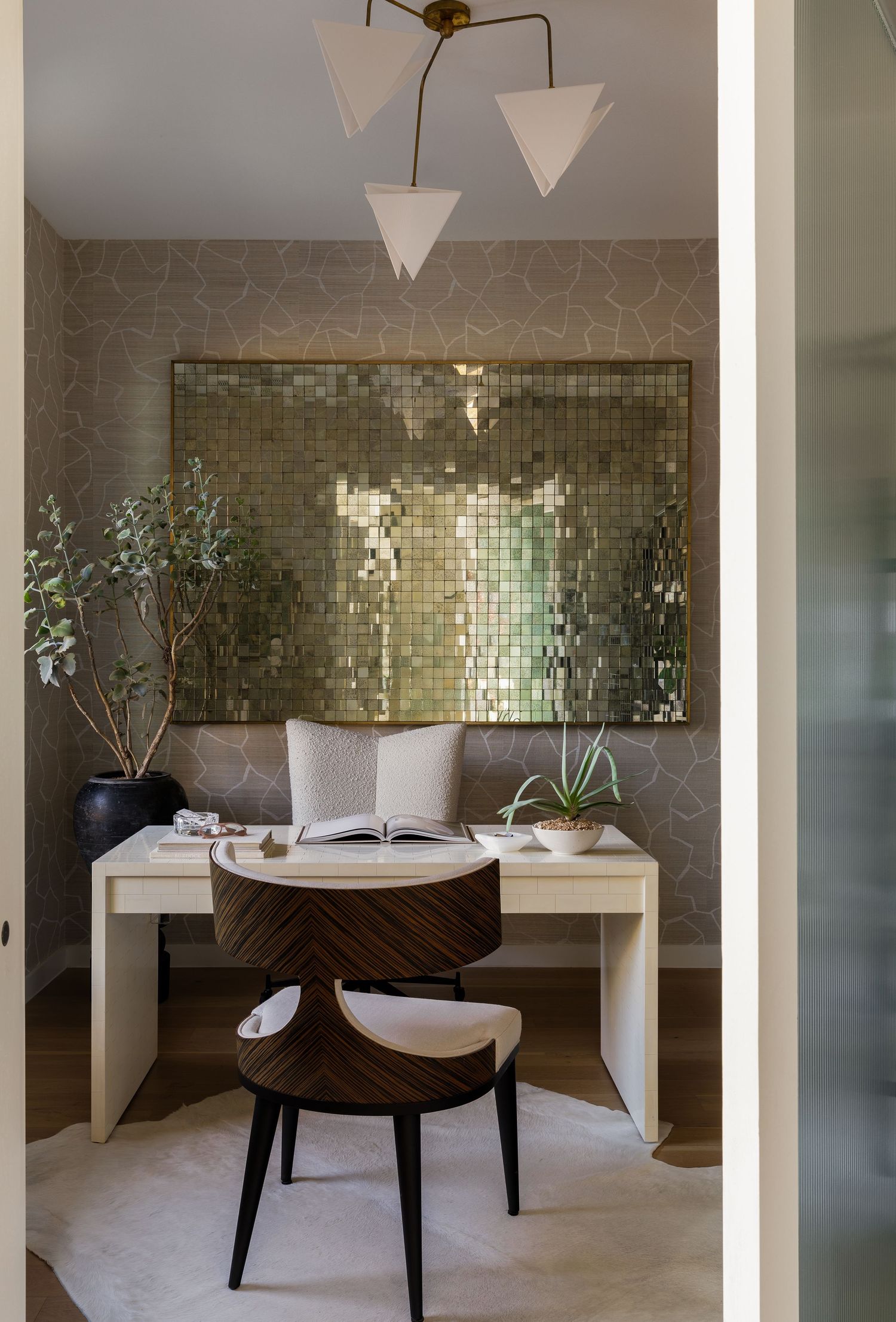 Modern home office nook featuring metallic tile wall art, geometric pendant lights, and sleek white desk with wooden chair decor.