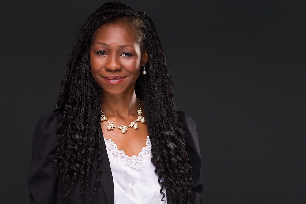 Professional headshot portrait against a dark background wearing a white top and pearl necklace.