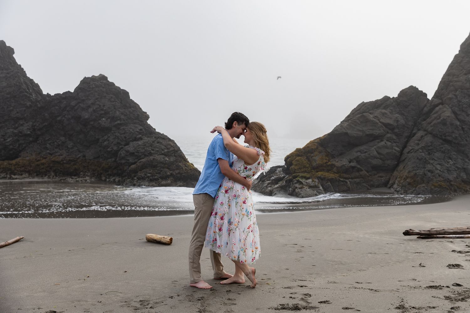 Couple embraces romantically on a dramatic Oregon Coast beach under an overcast sky.