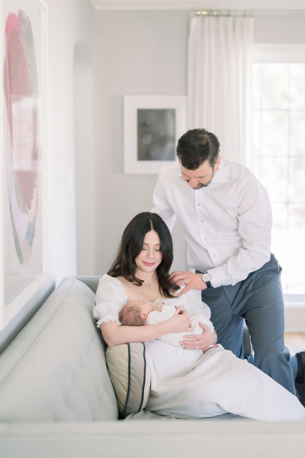 A tender moment captured in a bright living room as parents share a quiet moment with their newborn baby on a couch.