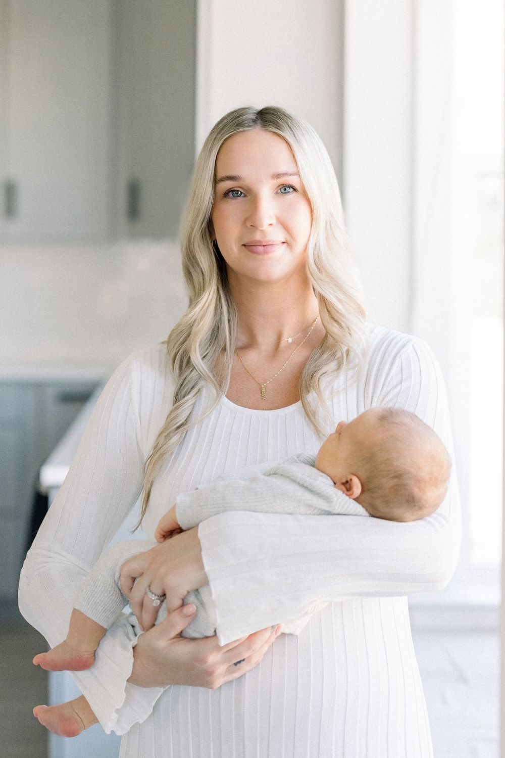 Parent in white clothing cradling a newborn baby in a bright, minimalist setting.