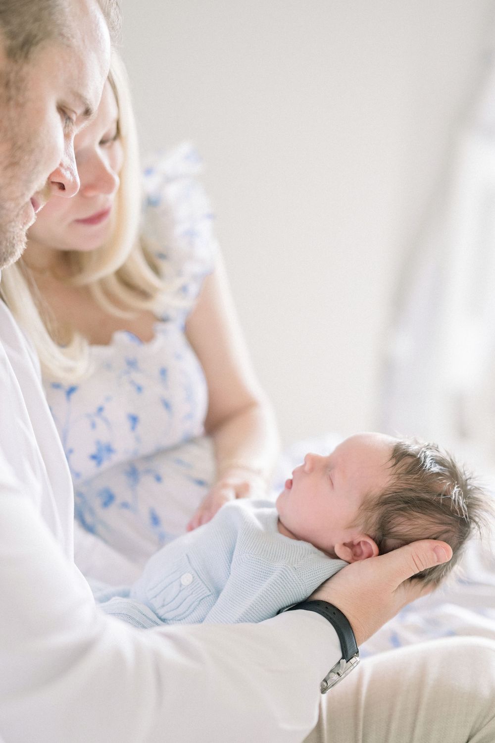 A gentle moment as a newborn baby is cradled in soft light while wearing a light blue outfit.
