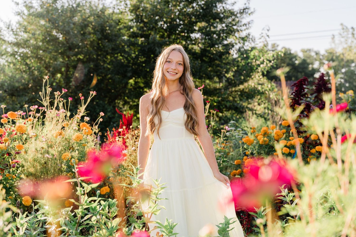 Perrysburg High School senior poses in a garden in late summer with colorful blooms in a flowy white dress for her photo session.
