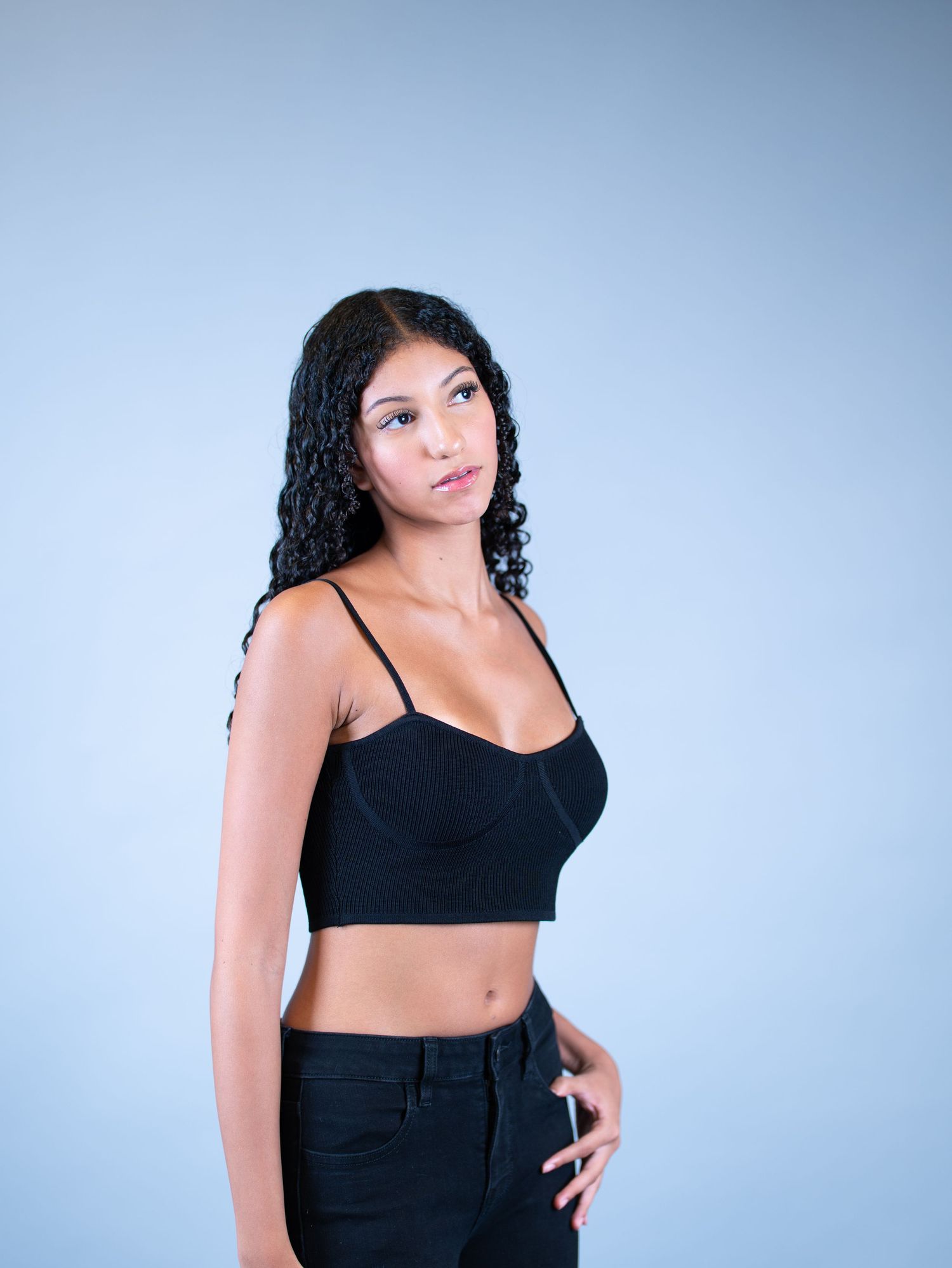 A stylish portrait series featuring poses in curly hair and black top against a light background.