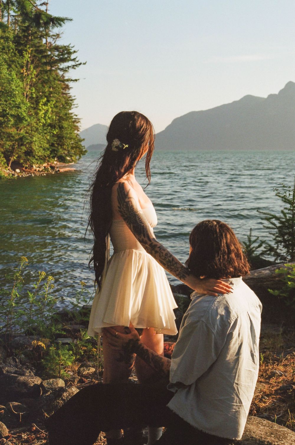 Two people enjoying sunset views over mountain lake from shoreline.