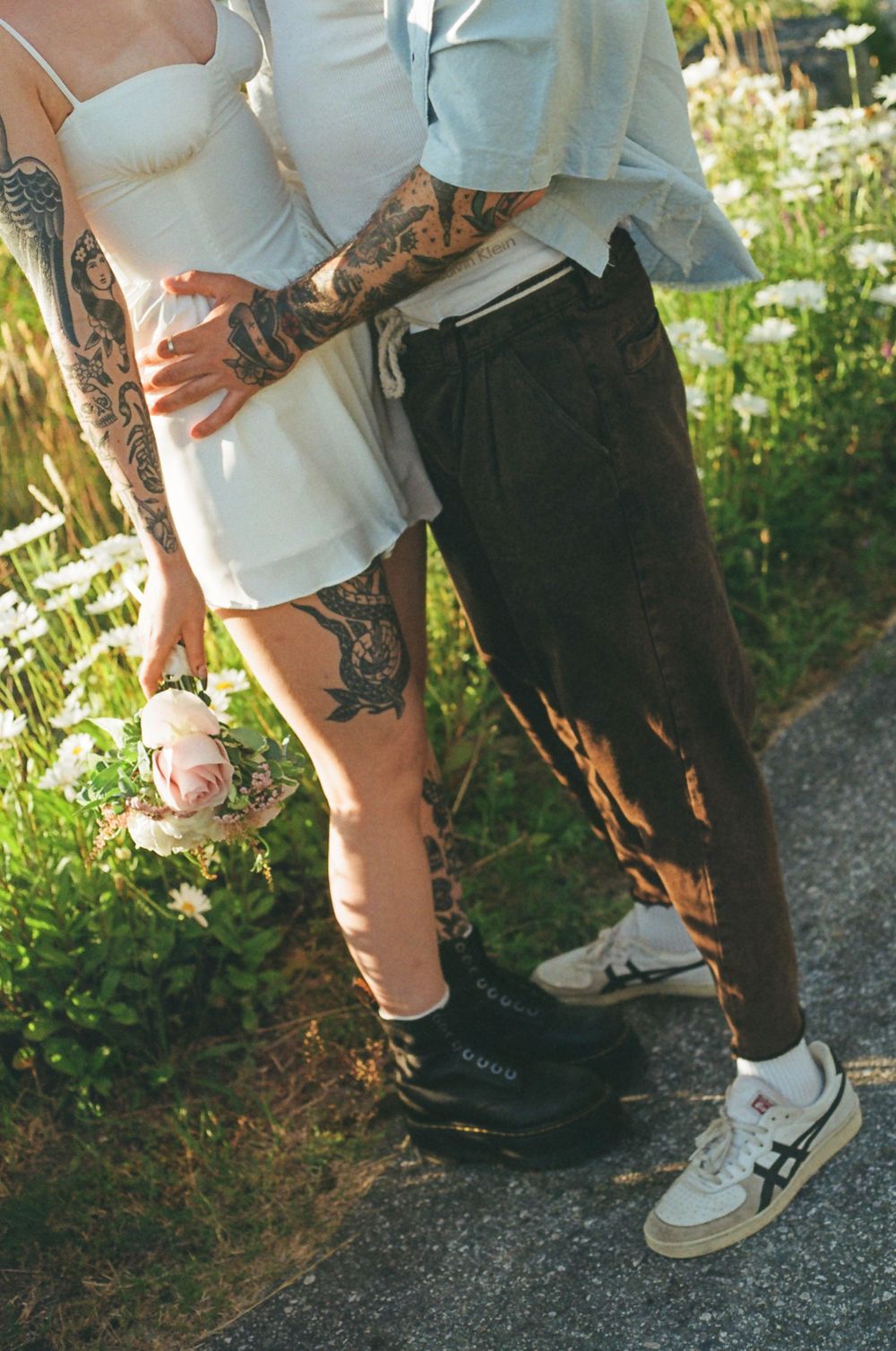Detail shot of tattoos and white sneakers on a gravel path.