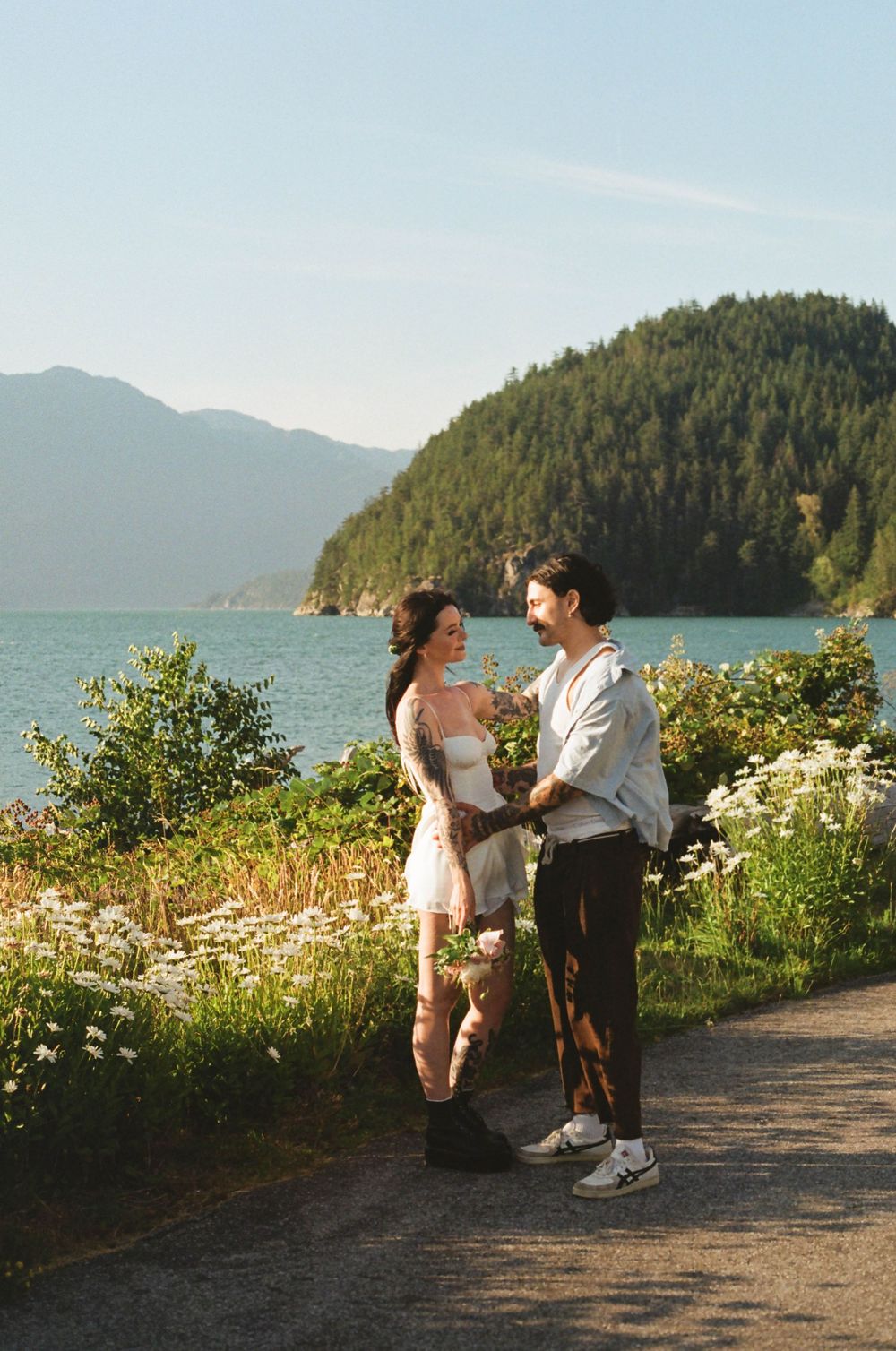 Couple sharing intimate moments on a coastal trail with mountain and ocean views.