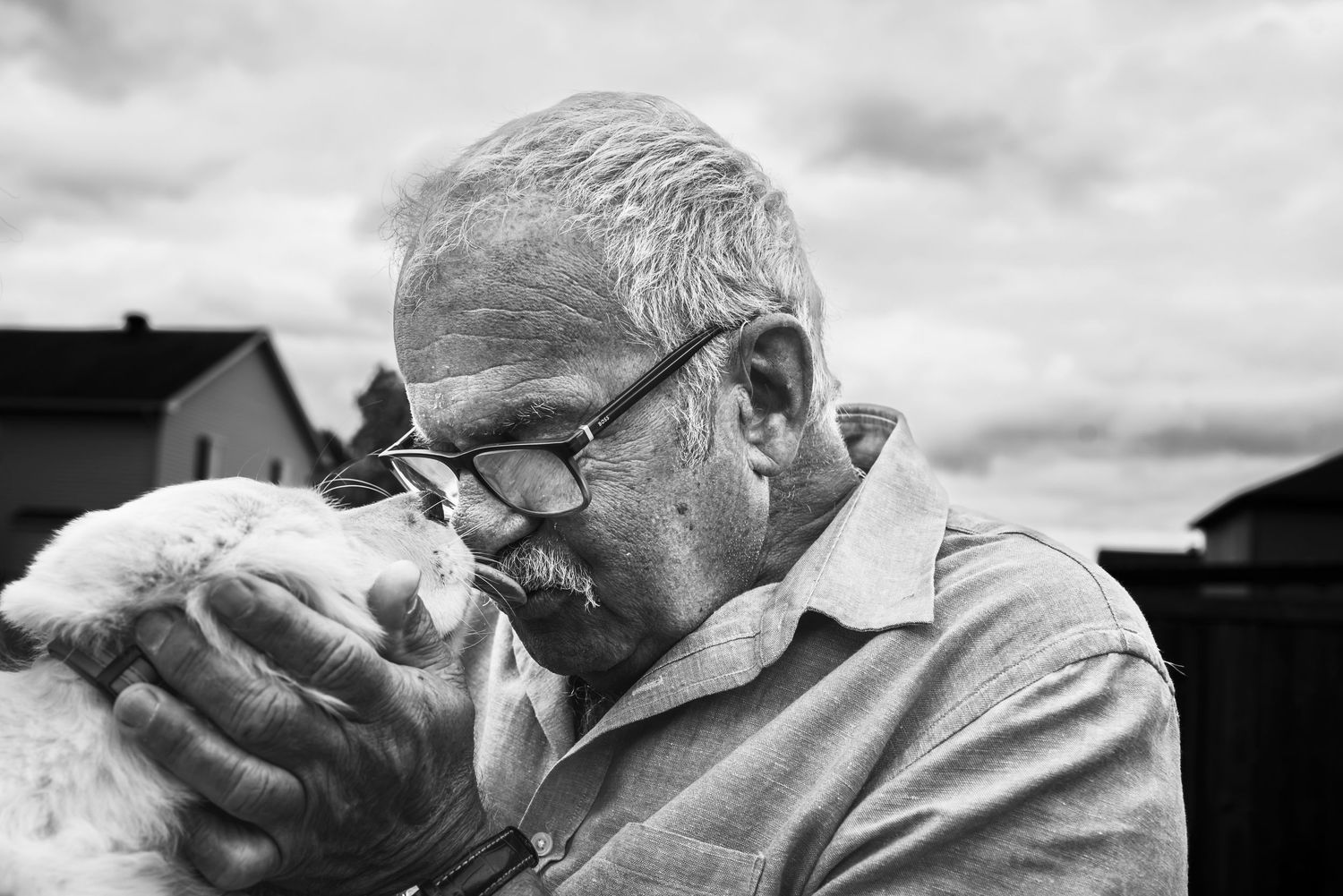 A man with grey hair leans into a puppy as it licks his face.