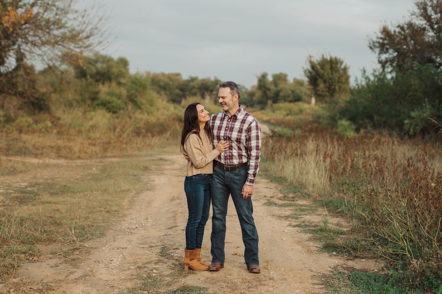 A romantic couple embraces on stone steps in a garden setting during golden hour.