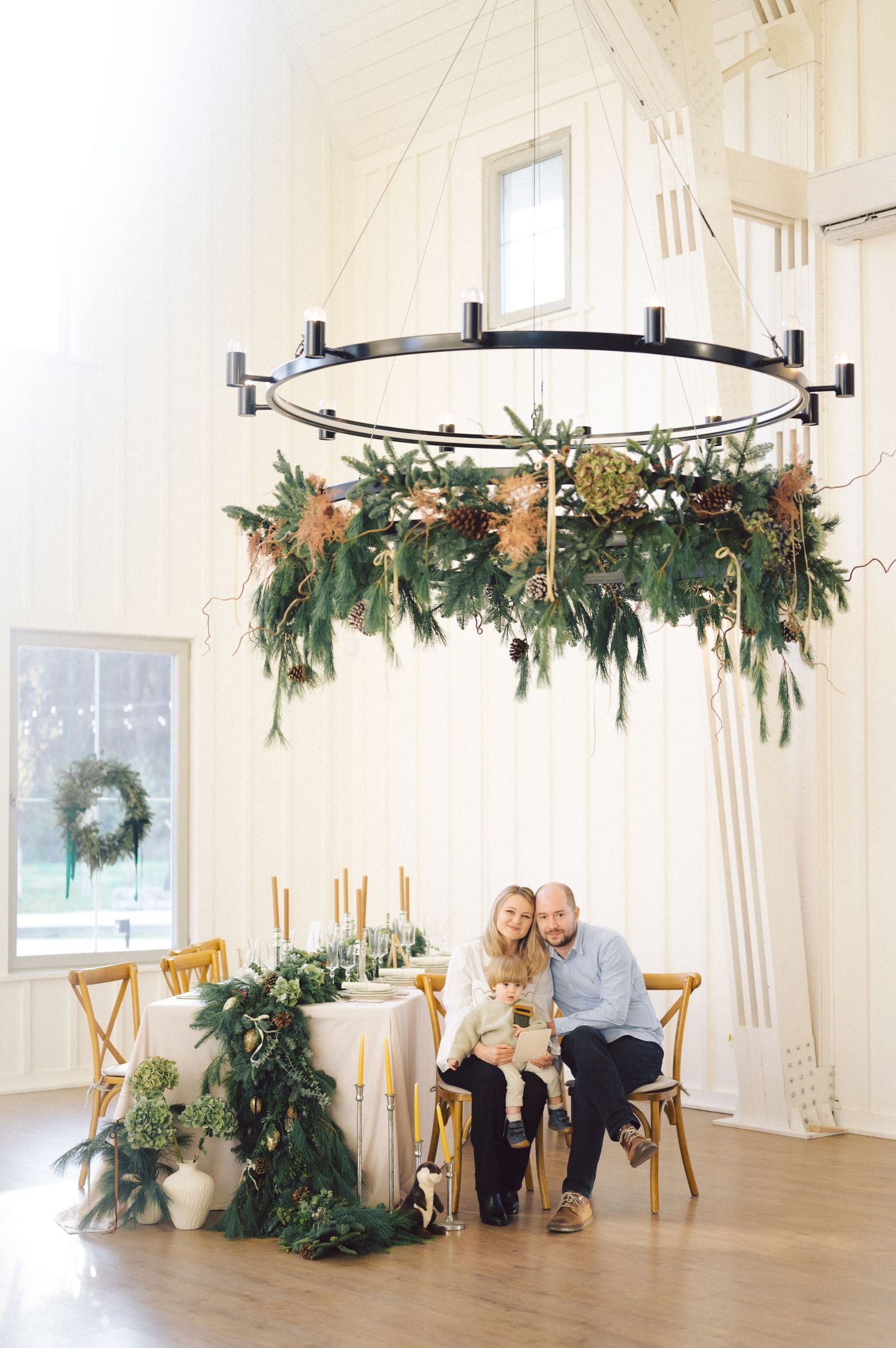 Modern light-filled studio space with circular chandeliers decorated with evergreen garlands and seasonal decor.