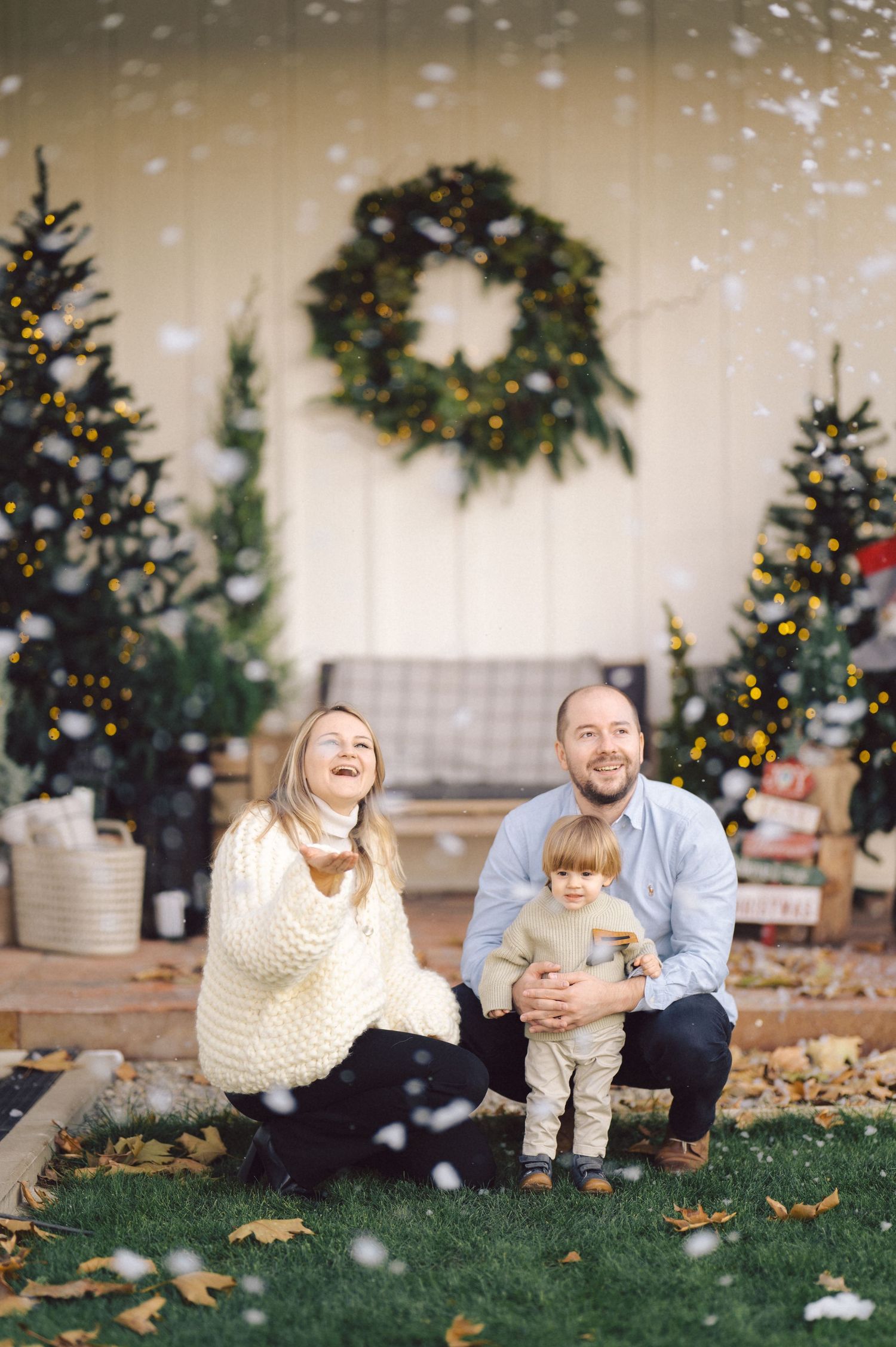 Family enjoying holiday photos in front of decorated Christmas display with falling snow effects and festive wreath.