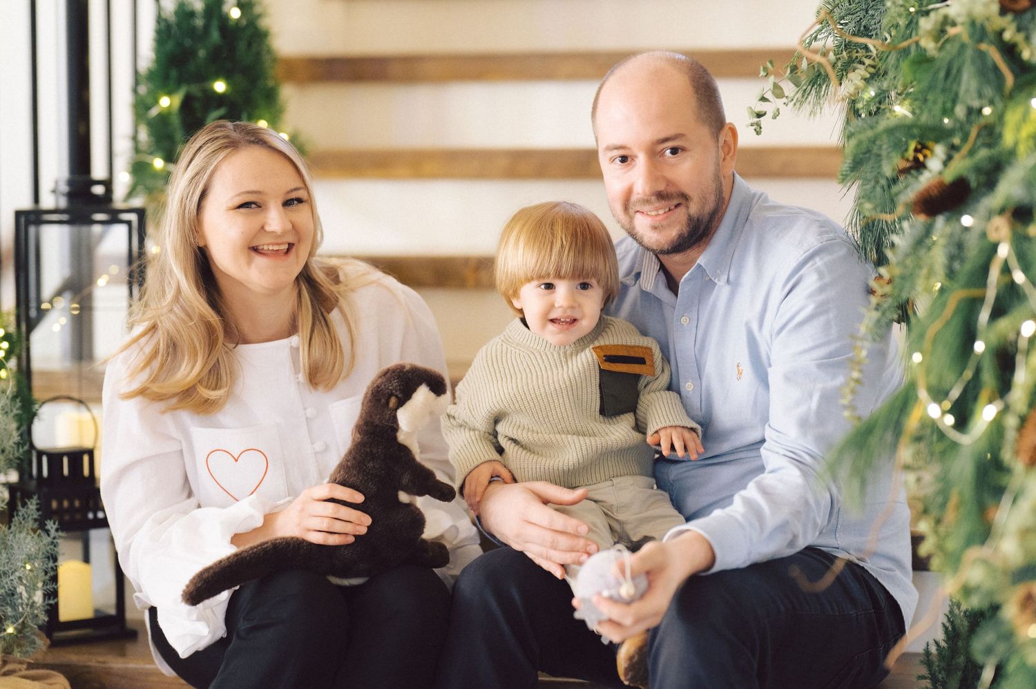 Family relaxes together on white couch under festive garland and decorative lights.