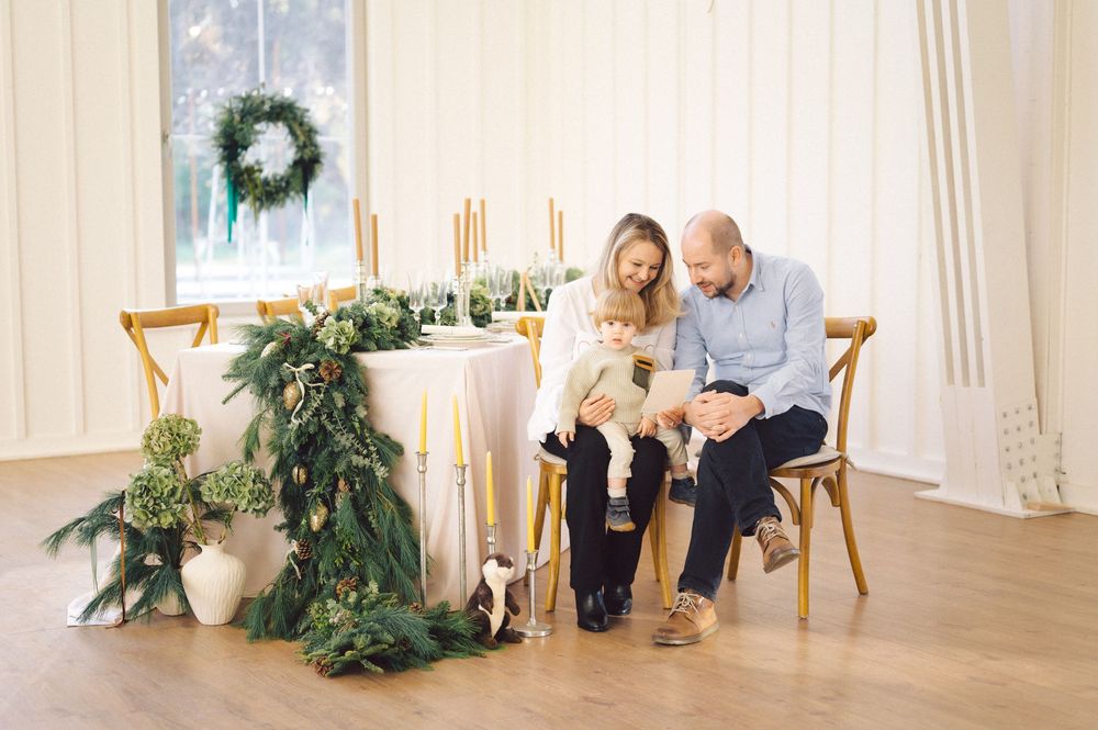 Two people seated in chairs sharing a cozy moment near an elegant holiday table with greenery and candle decorations.