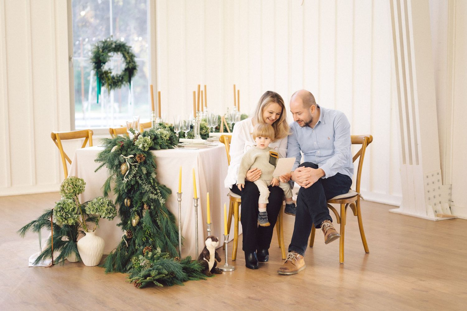 Two people seated in chairs sharing a cozy moment near an elegant holiday table with greenery and candle decorations.