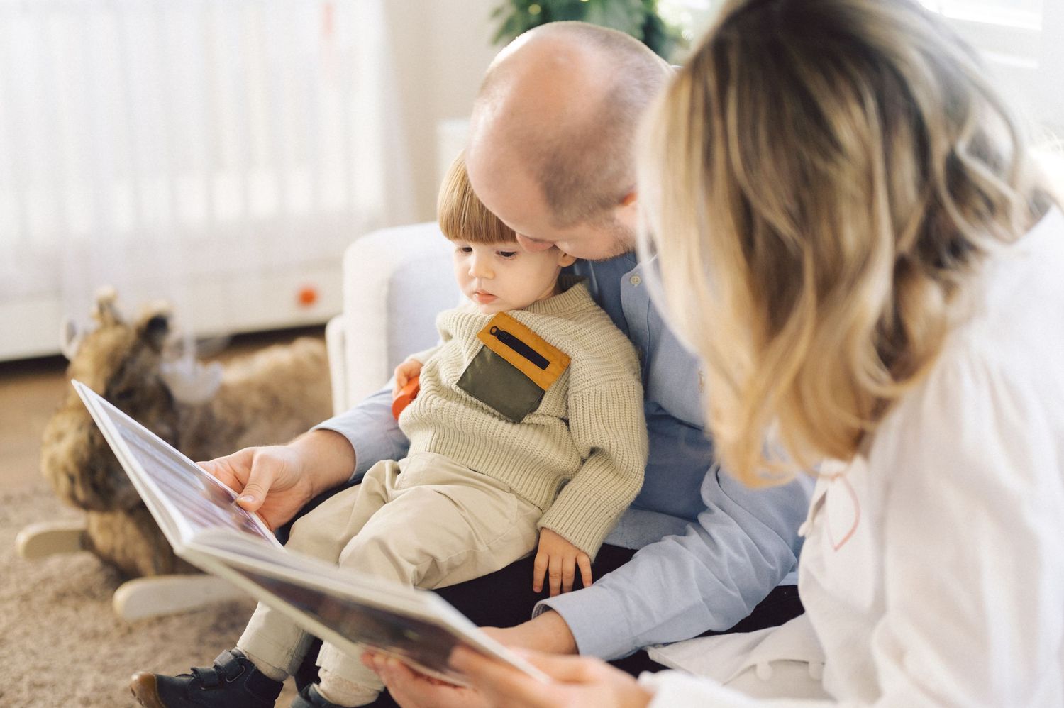 Family reading together on a cozy white couch while snuggling with their pet dog at home.