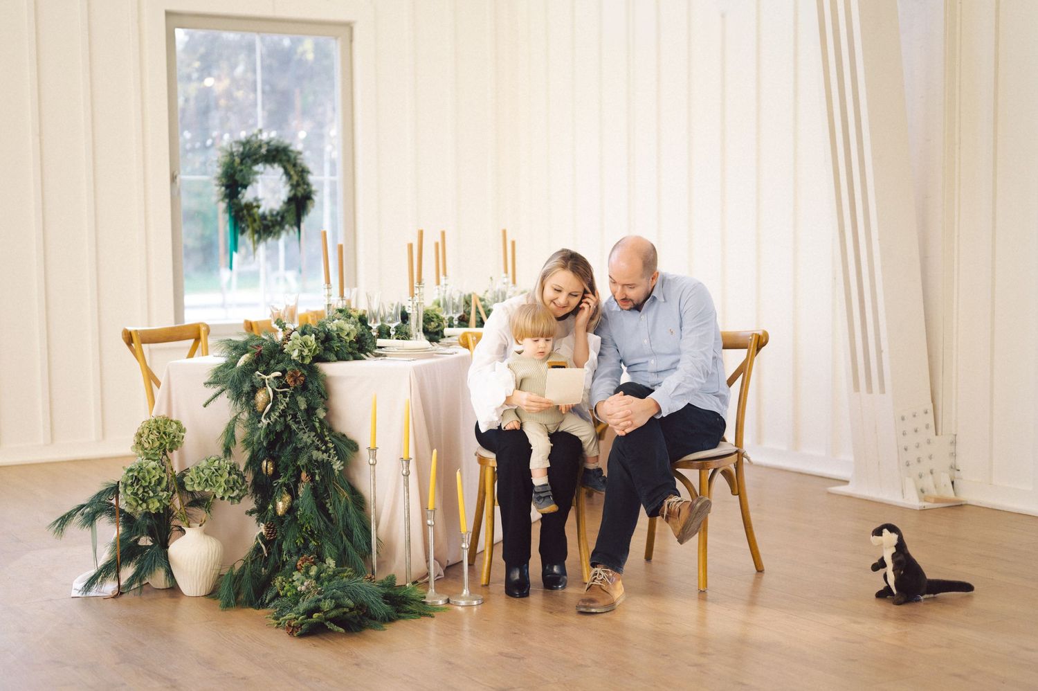 Elegant holiday scene with candlelit dinner table decorated with greenery and a small penguin decoration on wooden floor.