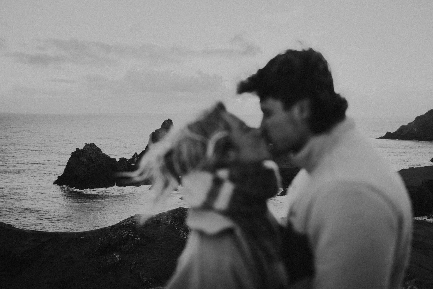 Black and white photo of couple running along rocky shoreline at sunset.