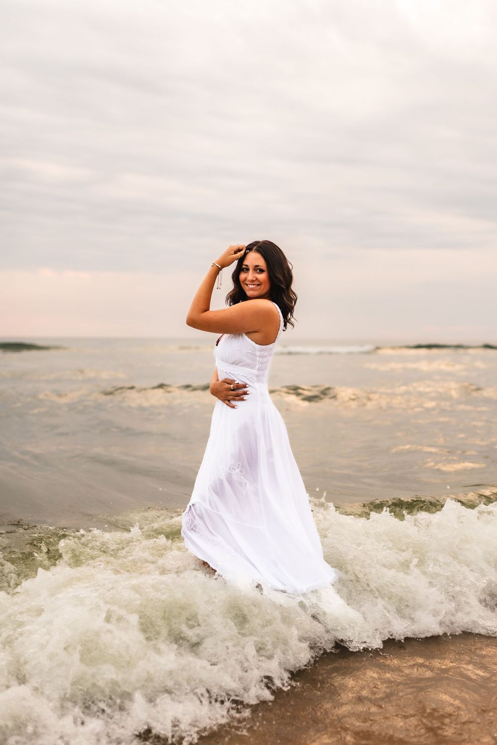 High school senior posing in a dress in the waves of Hoffmaster Beach.