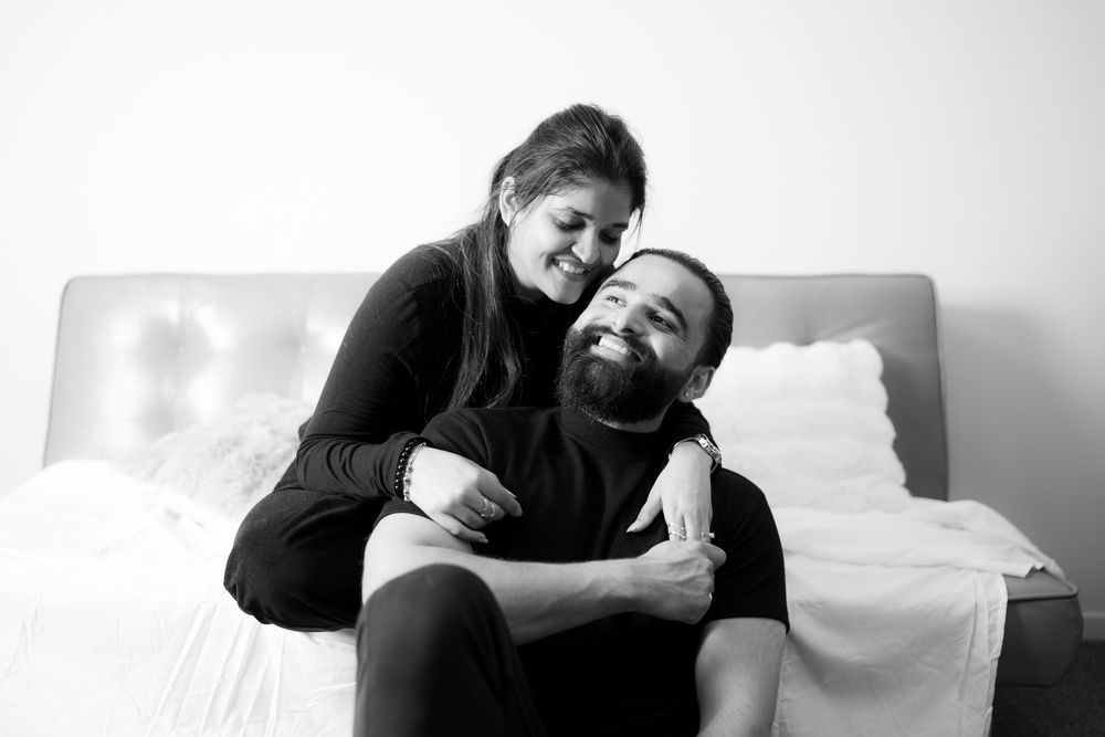 Black and white photo of a couple embracing while sitting on a white couch.