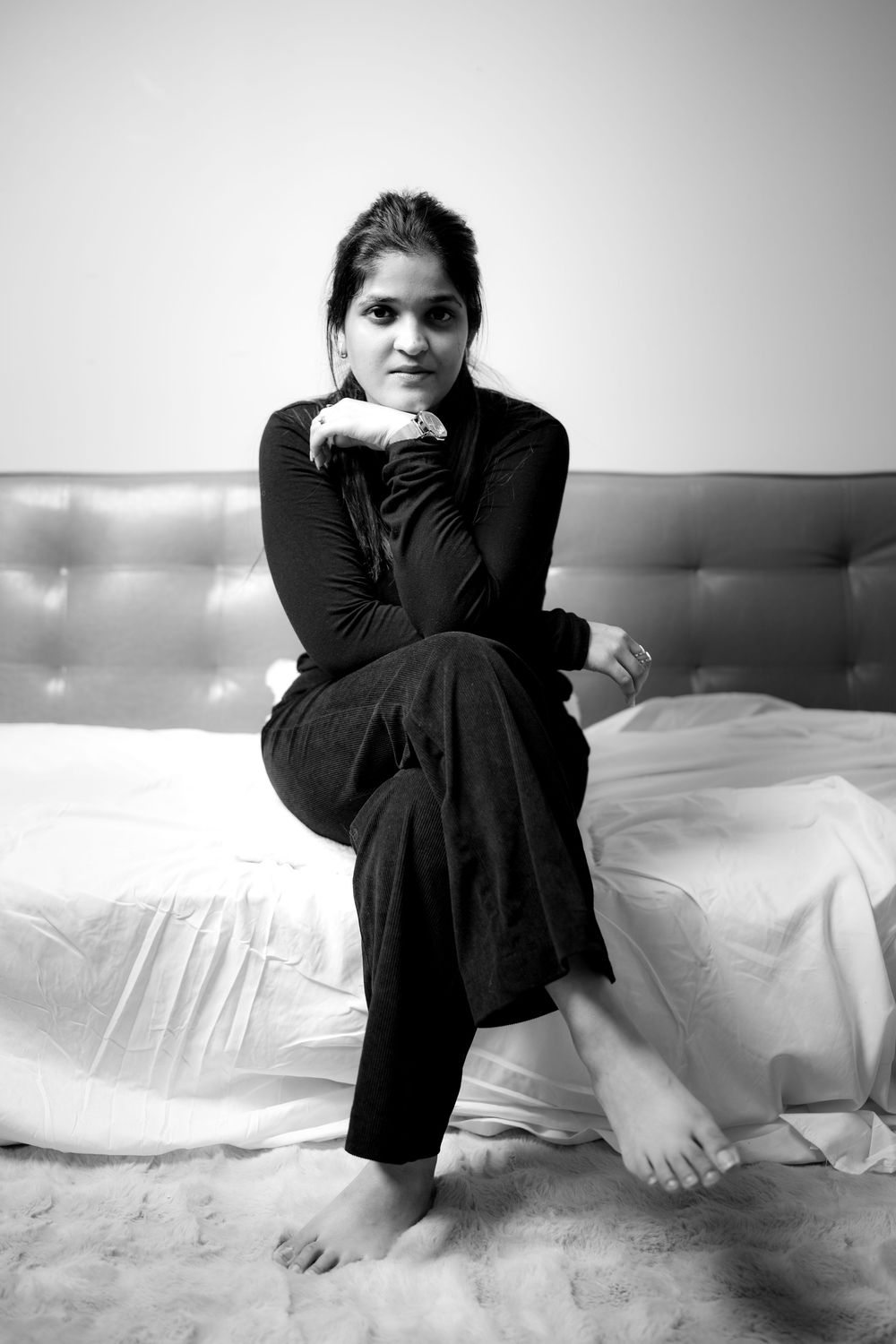 Black and white portrait of a person in dark clothing sitting casually on a white couch.