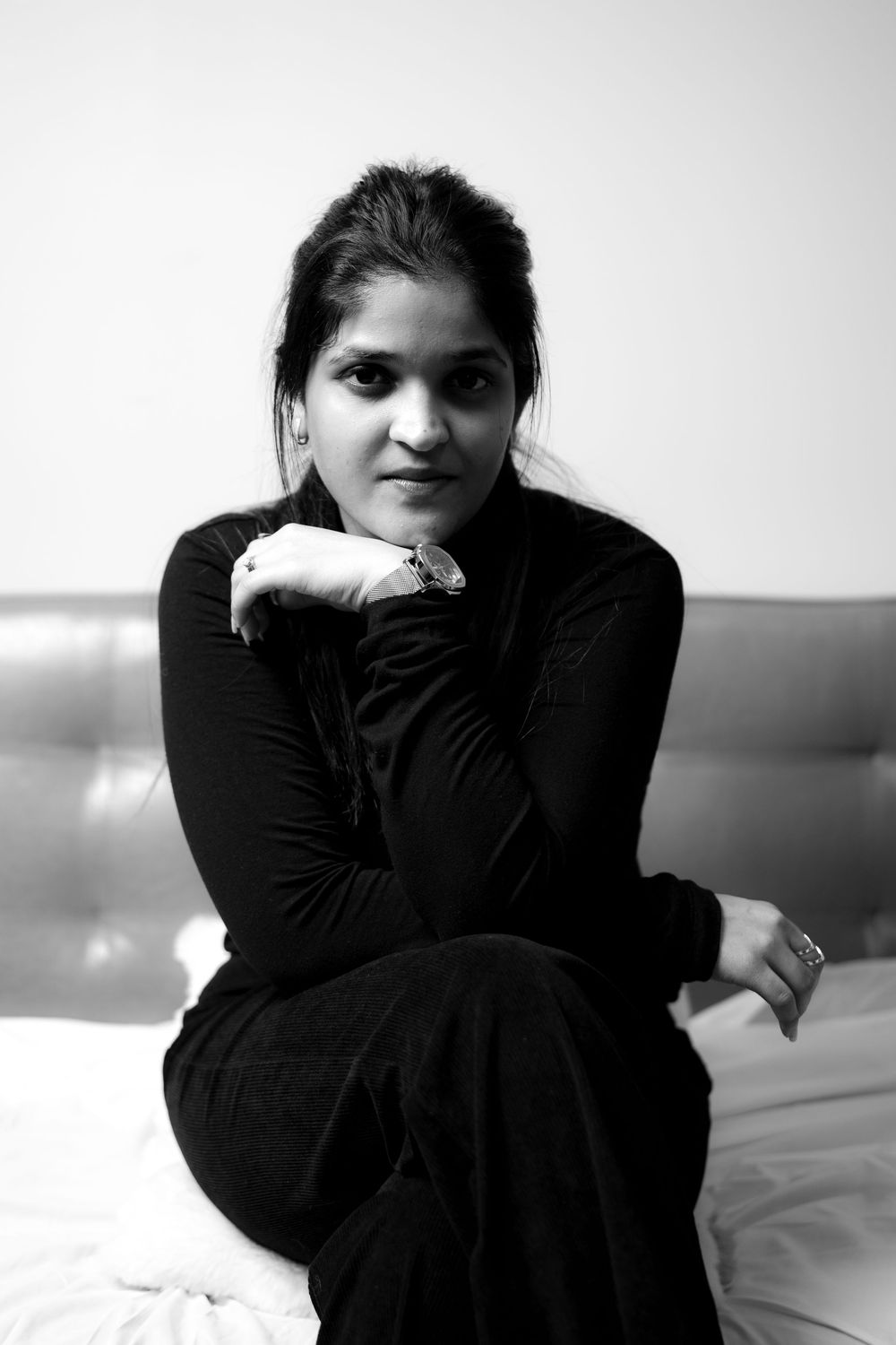Black and white portrait of someone posing in dark clothing while sitting on a light colored sofa.