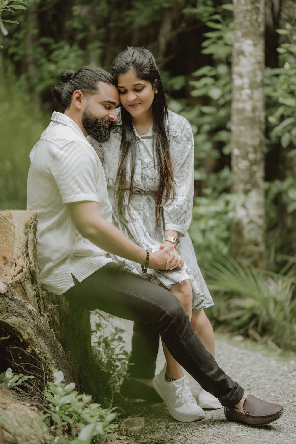 A romantic outdoor forest portrait of a couple sharing an intimate moment while sitting on a fallen log.