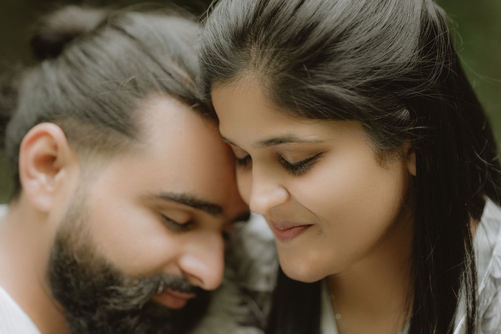 A romantic close-up portrait of a couple gently touching foreheads while smiling with their eyes closed.