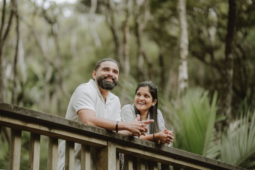 A couple enjoys drinks and conversation together on a wooden deck overlooking a lush forest landscape.
