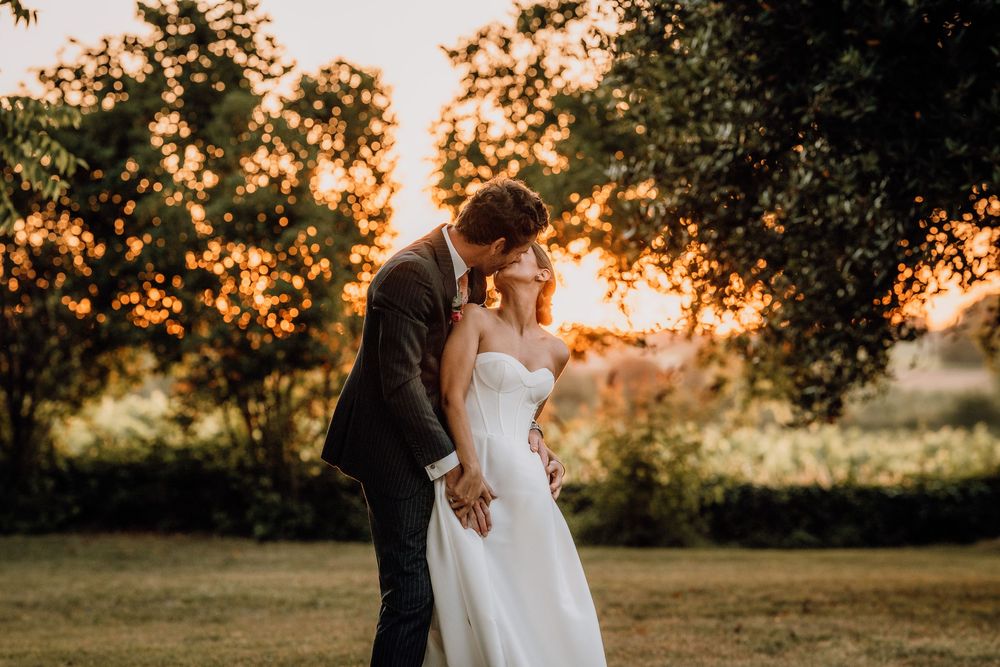 A romantic couple in wedding attire embrace during a golden sunset in a lush garden setting.