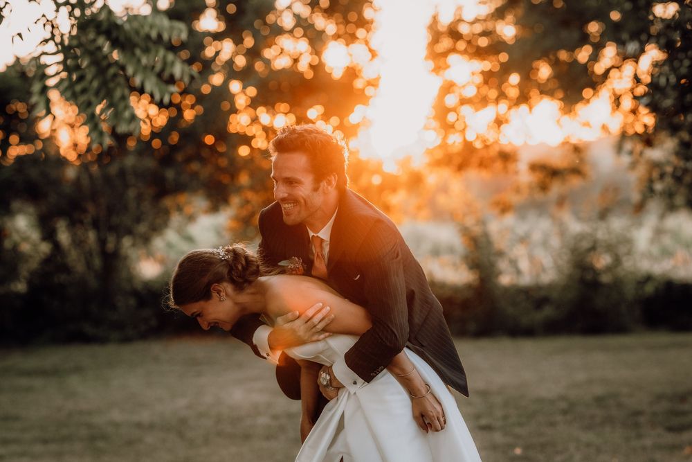 A couple embraces in a romantic dip pose during golden hour sunset in a garden setting.