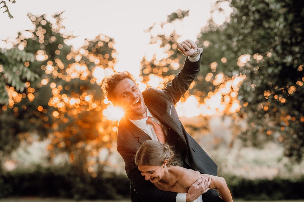 Silhouetted couple dancing together during golden sunset in nature with backlit trees creating magical setting.